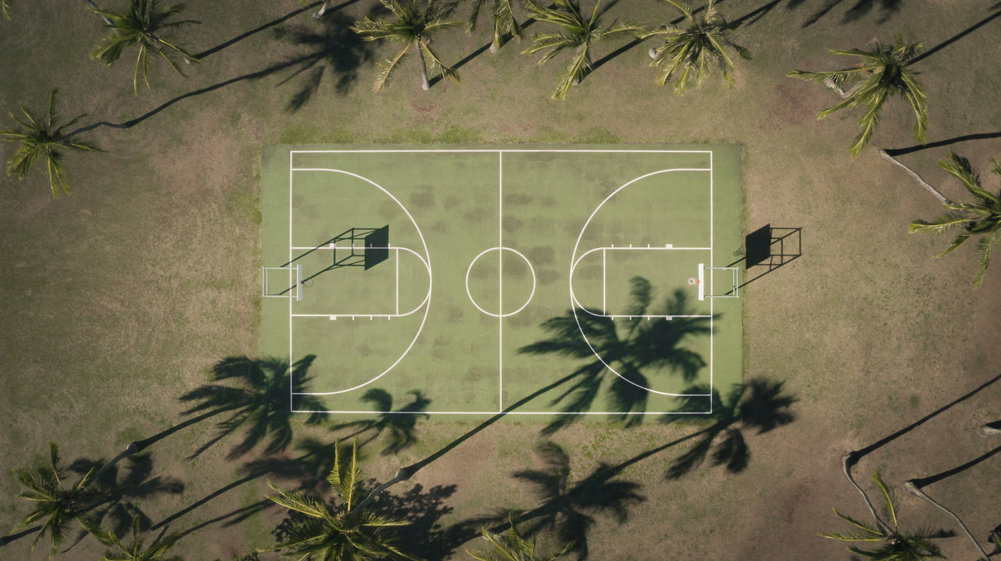 Aerial view of a basketball court surrounded by palm trees and their shadows at Kuliouou Beach Park in Oahu, Hawaii.