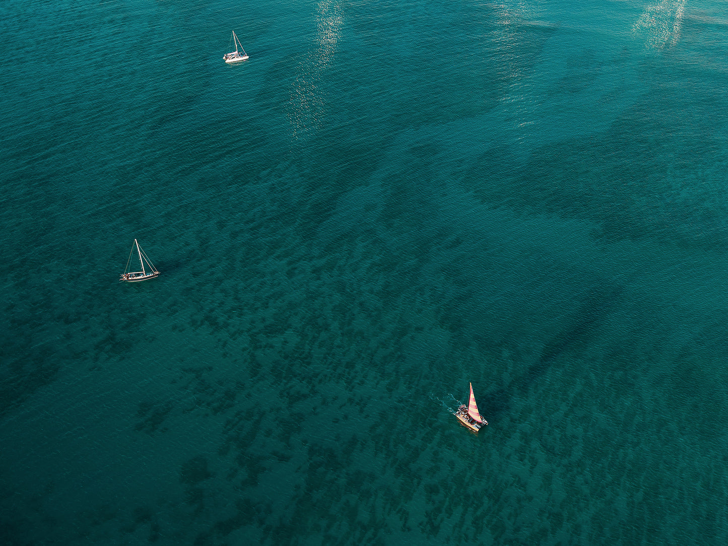 Aerial view of Waikiki's deep blue ocean and the coral underneath it along with three sailboats gliding across the water.